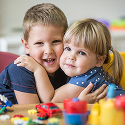 Two children smiling together during classroom playtimeChild concentrating while writing during classroom activity