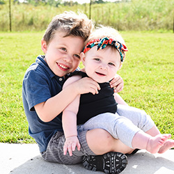 Boy with little sister on his lap outside sitting on sidewalk