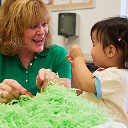 Teacher and young girl playing at sensory table with green shavings of paper
