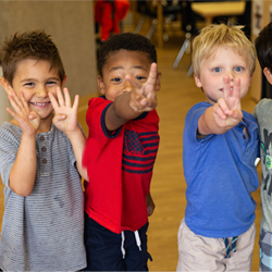preschool children smiling together in the classroom showing numbers with their fingers