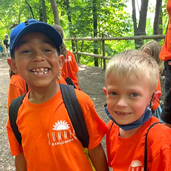 Two children wearing backpacks smiling during outdoor summer camps activity