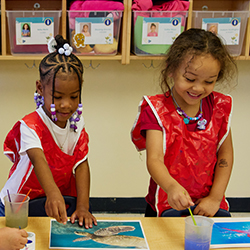 two girls with painting smocks on working on a water color painting activity