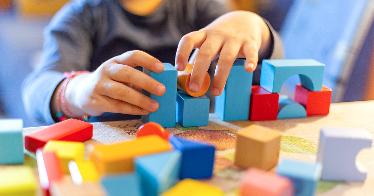 A child’s hands stacking colorful wooden blocks on a table.