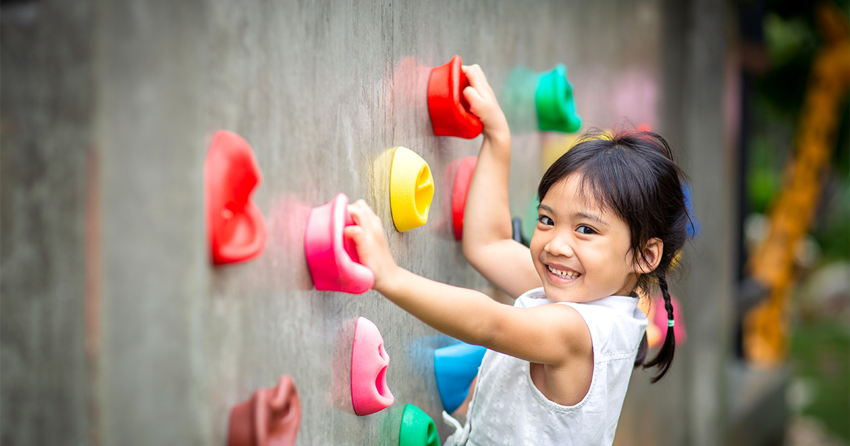 Child climbing a wall with colorful handholds on a playground.